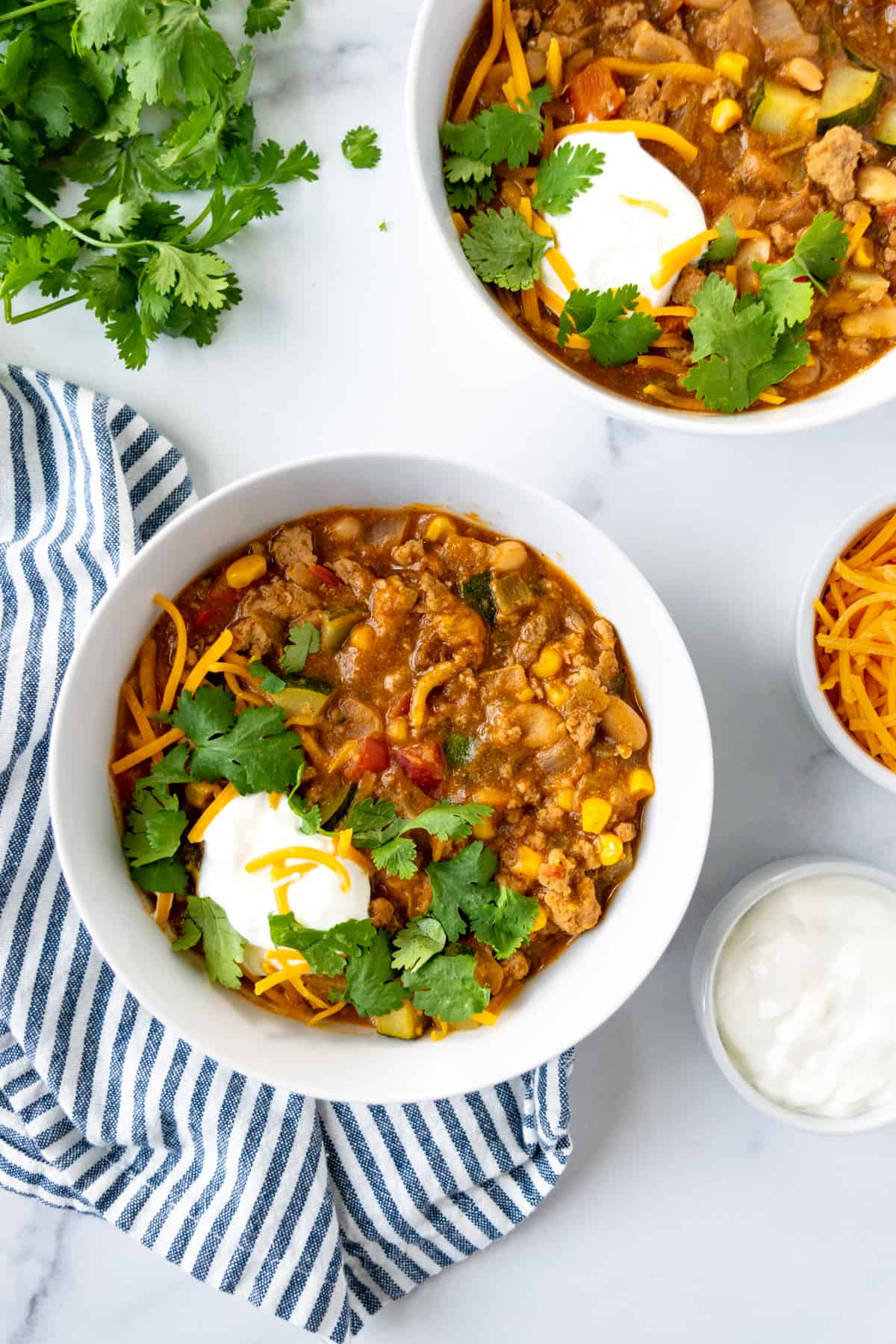 Stovetop Turkey and Vegetable Chili in 2 white bowls with cheddar cheese and sour cream.