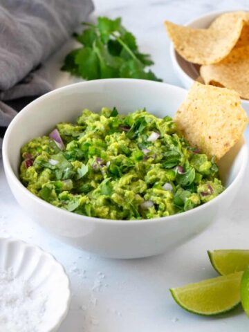 Classic Guacamole in a white bowl with a chip dipping in it.