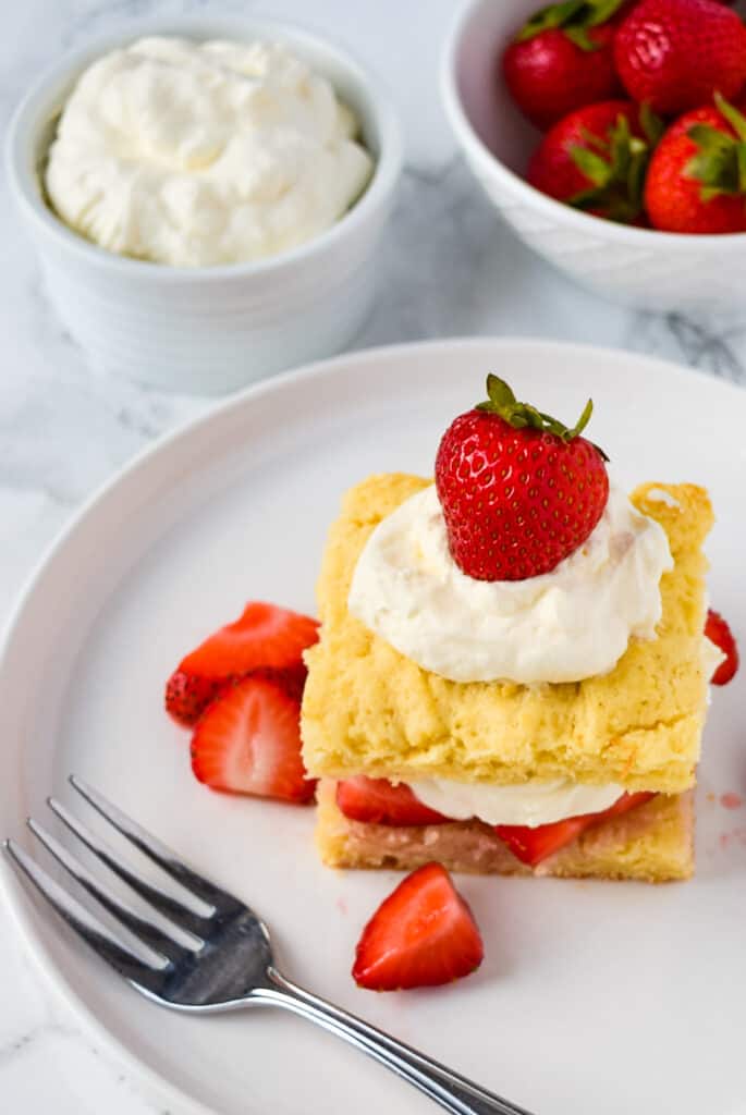 Easy Strawberry Shortcake on a plate with a fork with whipped cream and extra strawberries.