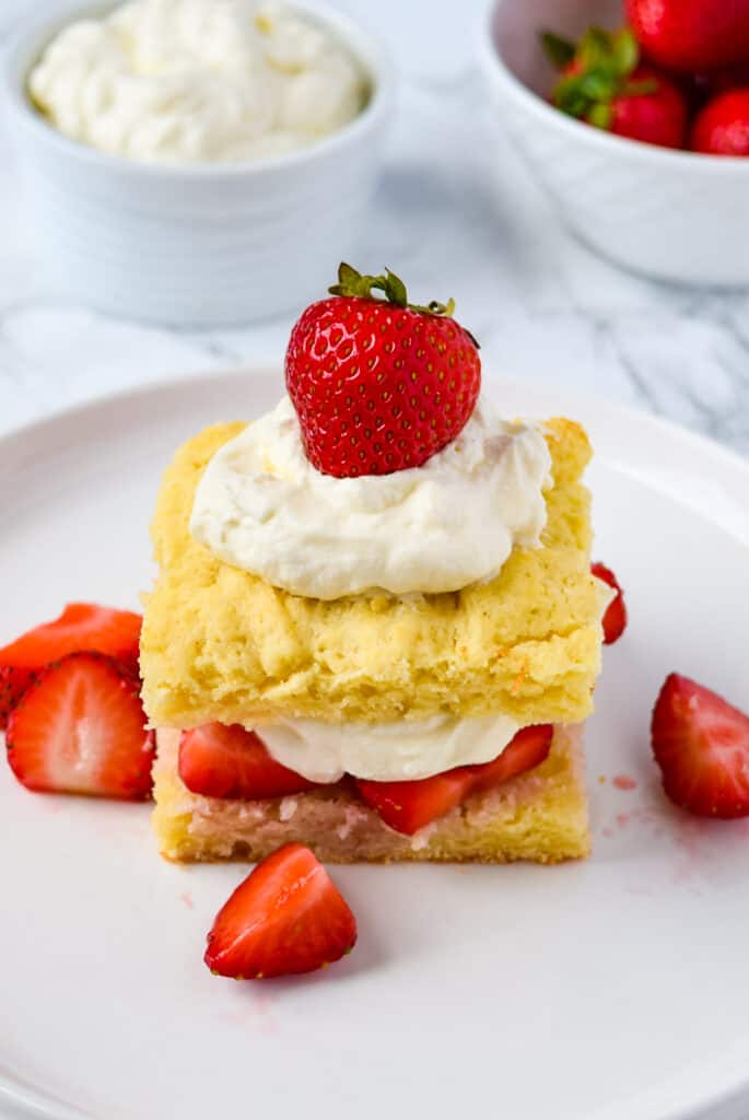 Easy Strawberry Shortcake on a plate with a small bowl of whipped cream and a bowl of strawberries in the background.