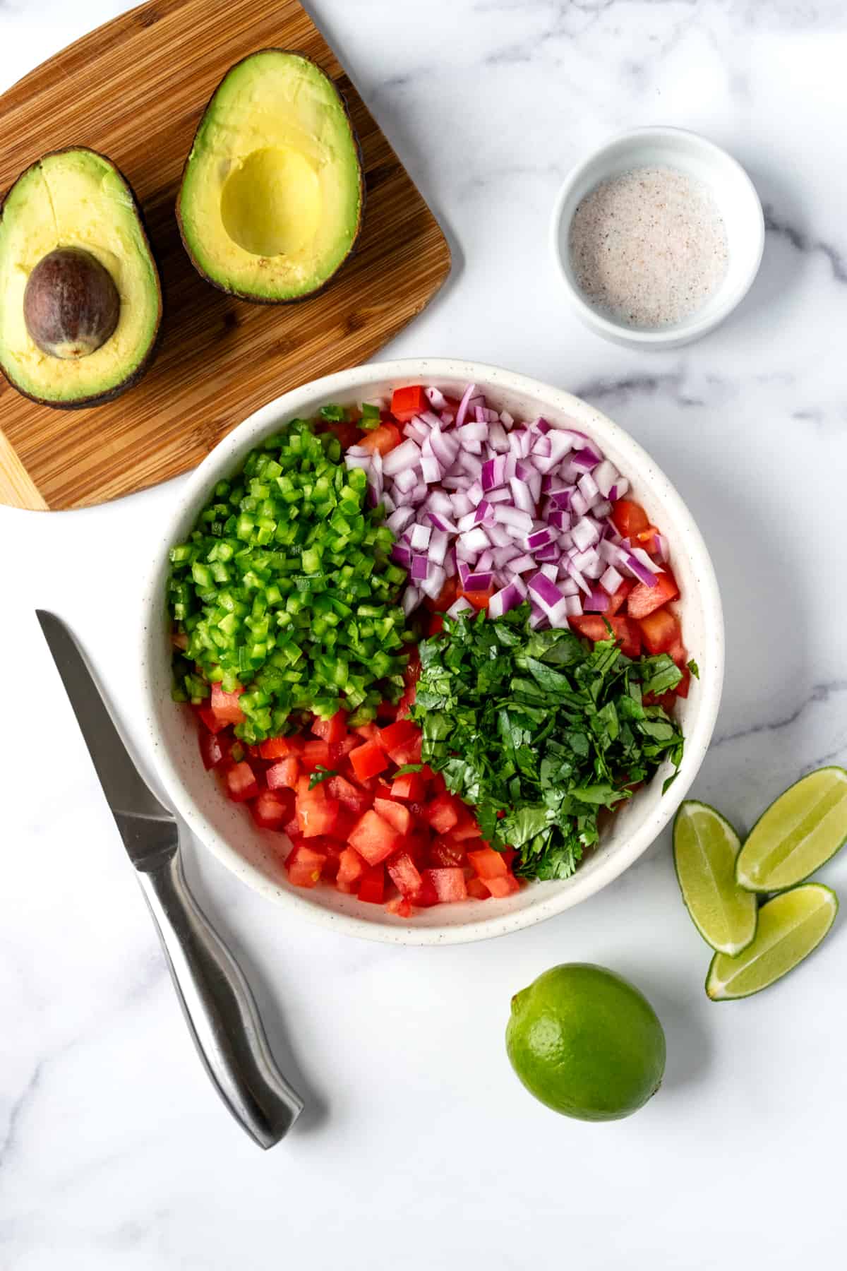 A white bowl with diced tomatoes, red onion, jalapeno, cilantro, lime juice, and salt.
