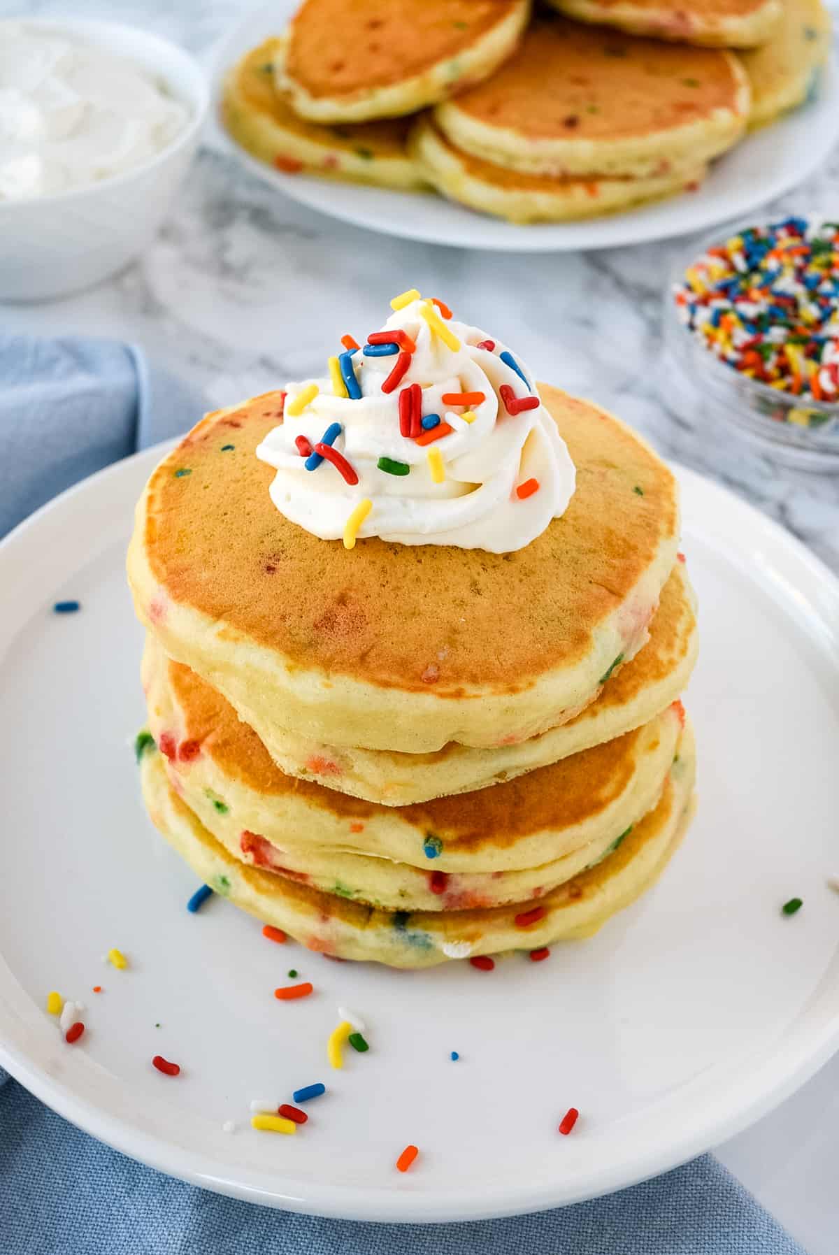 A Stack of Confetti Pancakes Topped with Whipped Cream on a White Plate.