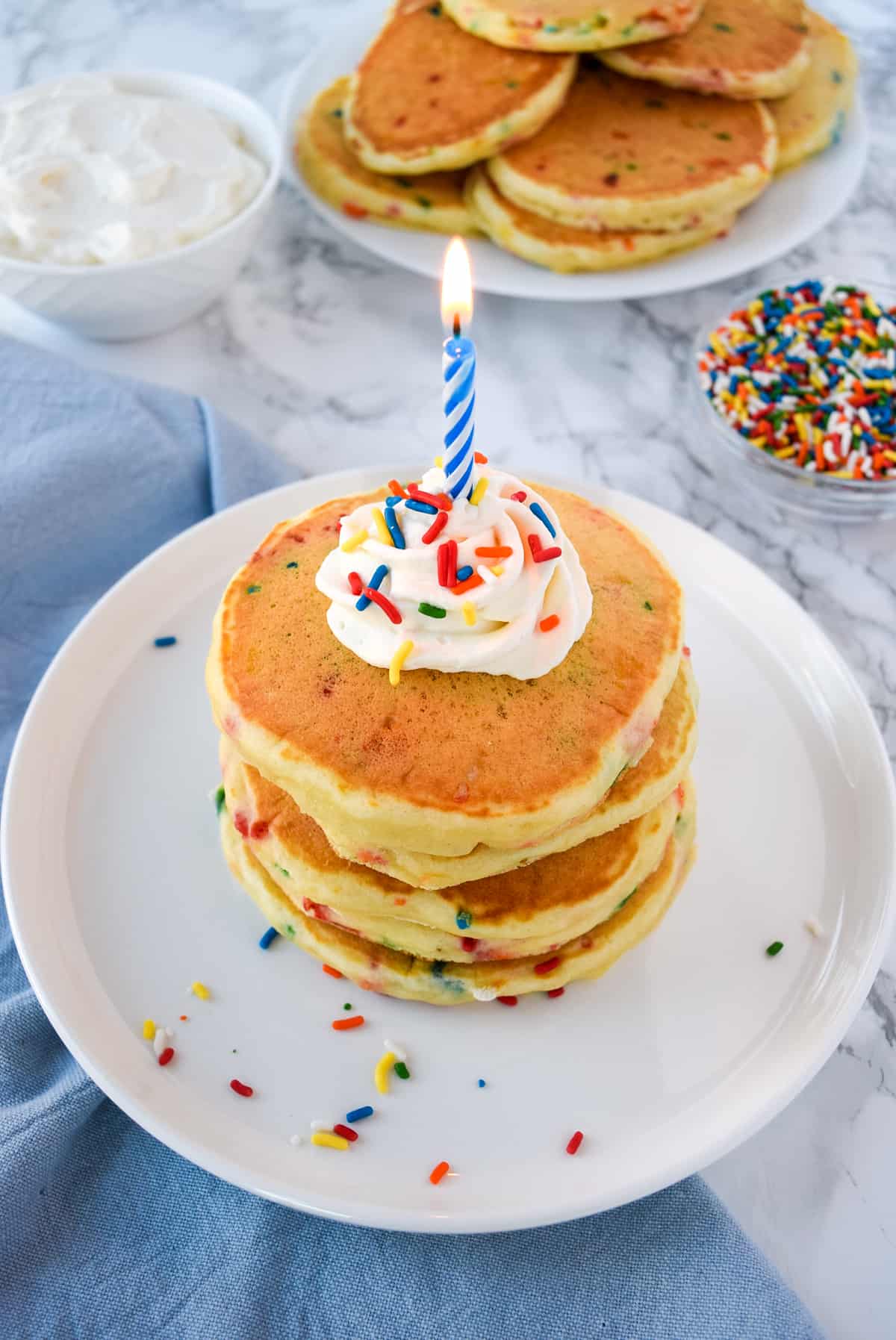 Stack of confetti pancakes with whipped cream and a birthday candle.