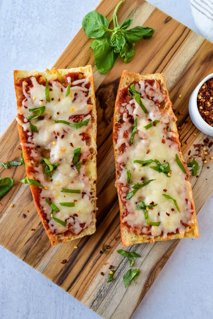 Air Fryer French Bread Pizza on a cutting board topped with basil.