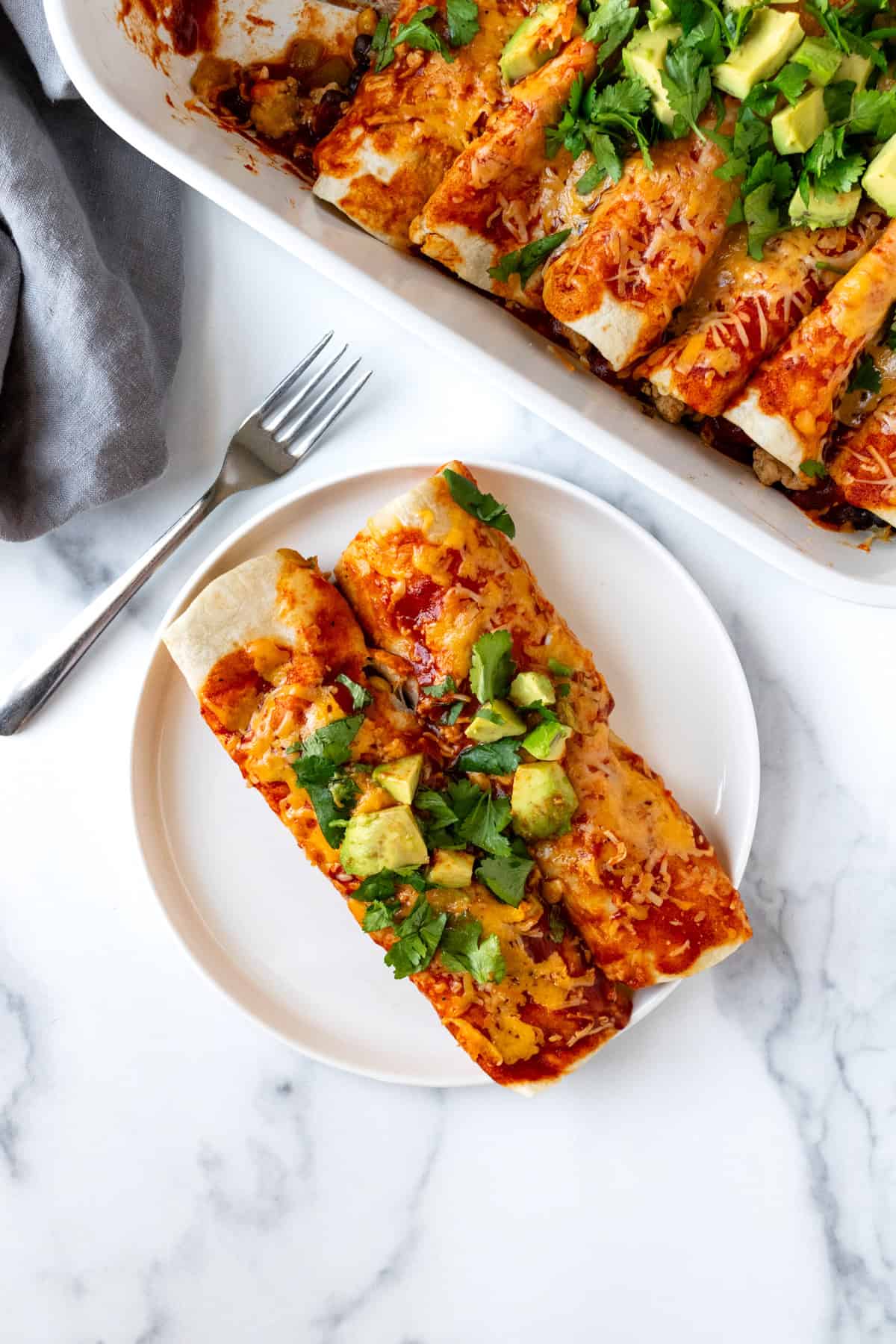 Two Ground Turkey Enchiladas on a white plate with a fork.