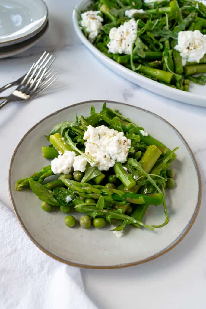 Spring Pea and Asparagus Salad with Ricotta on an appetizer plate with a platter of it in the background.