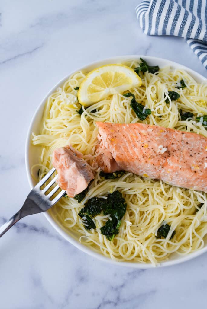 Lemon Kale Pasta with Salmon on a plate with a bite of salmon on a fork.