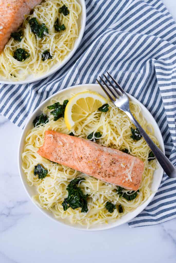 Lemon Kale Pasta with Salmon on a plate with a fork and lemon wedge.