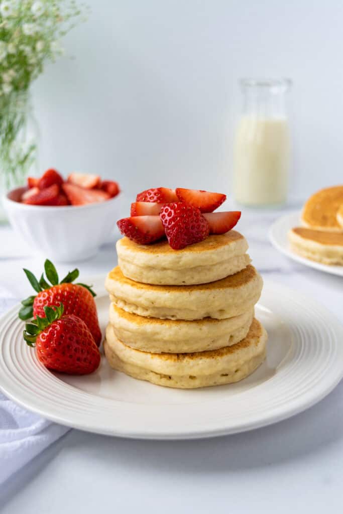 A stack of oat milk pancakes on a plate topped with strawberries.