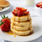 Stack of 4 oat milk pancakes topped with strawberries and maple syrup dripping down the sides.