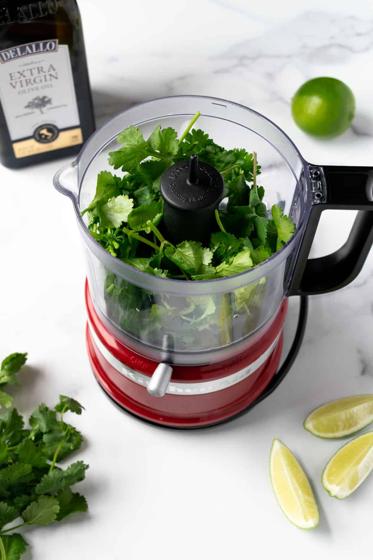 Cilantro in a small food processor on a table with limes and olive oil.