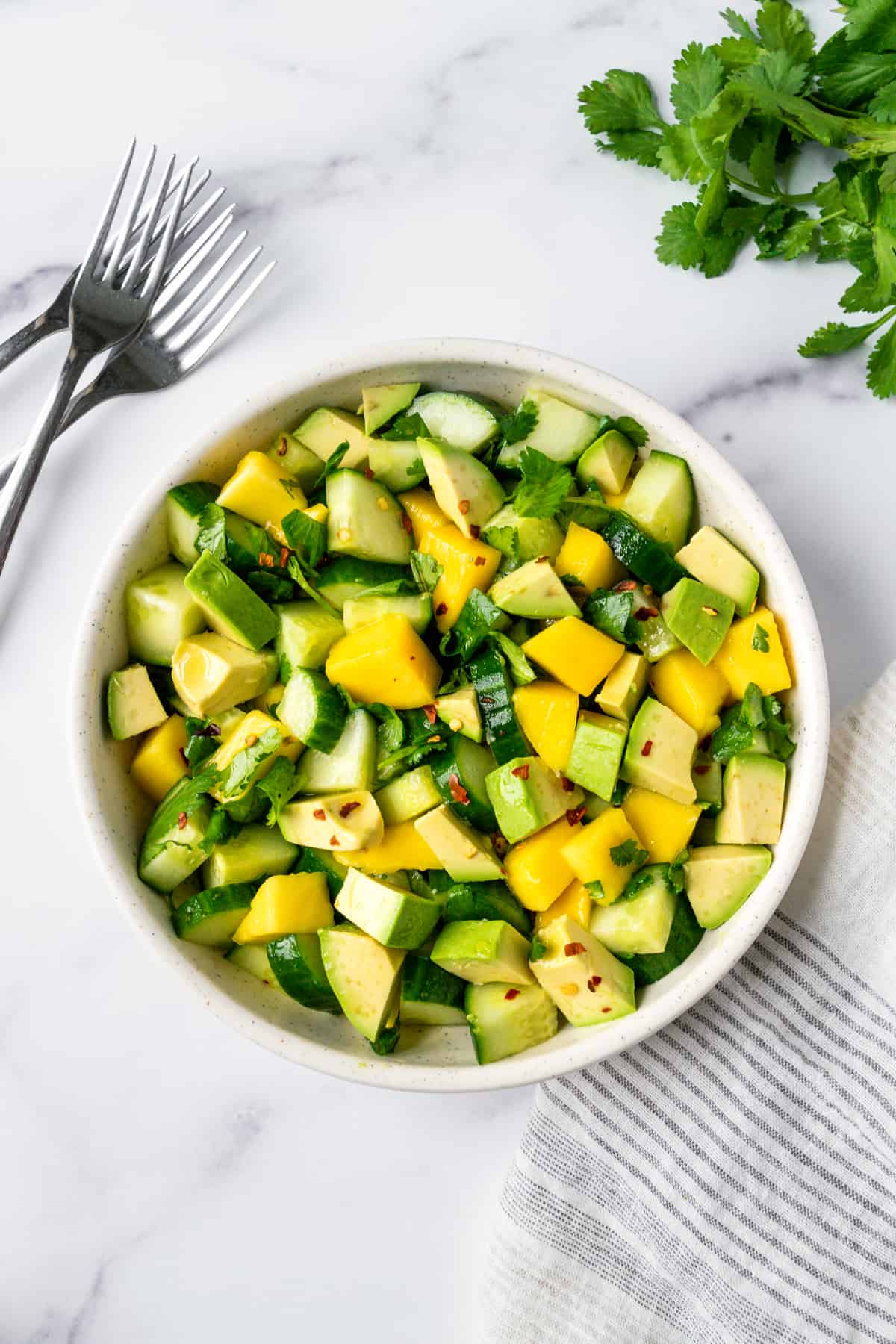 Cucumber Mango Salad with Avocado in a white bowl with a few forks next to it.
