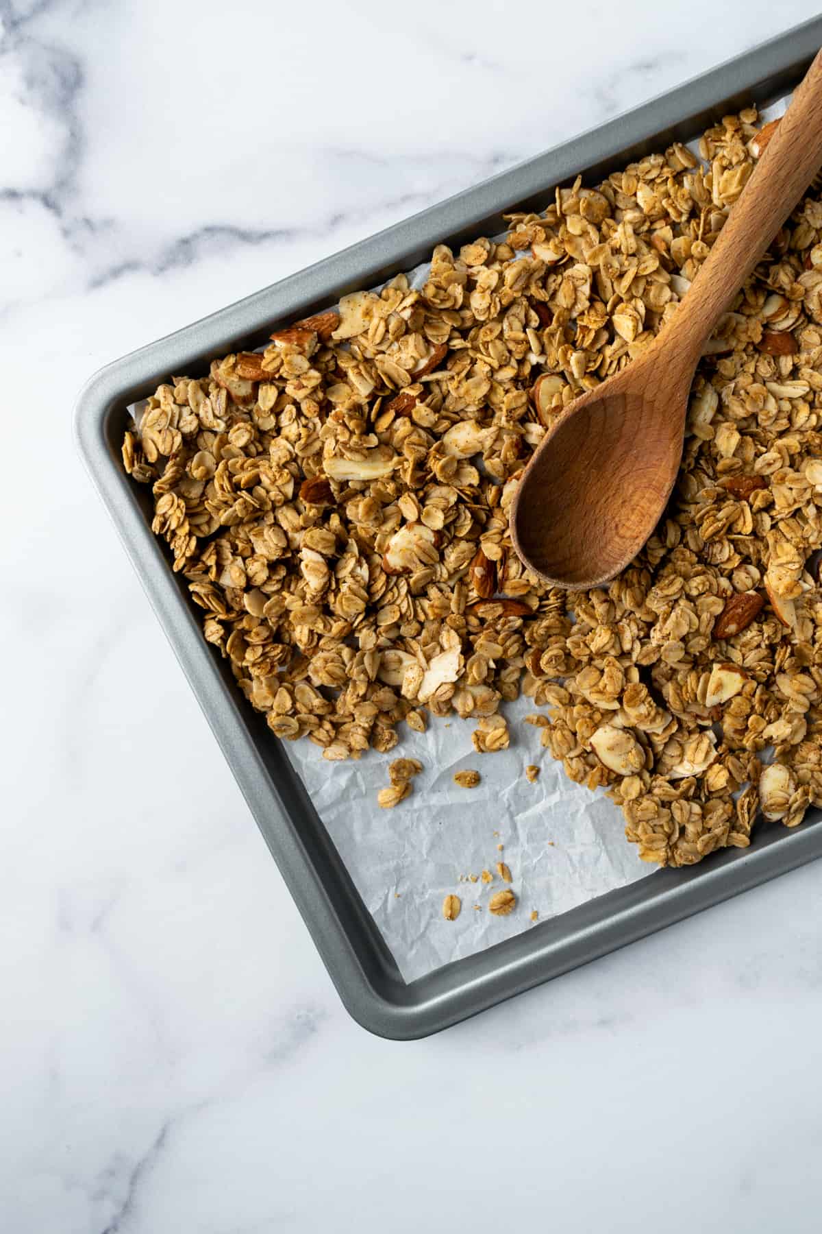 Almond Vanilla Granola on a baking sheet with a wooden spoon.