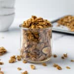 Almond Vanilla Granola in a jar on a table with some white bowls.