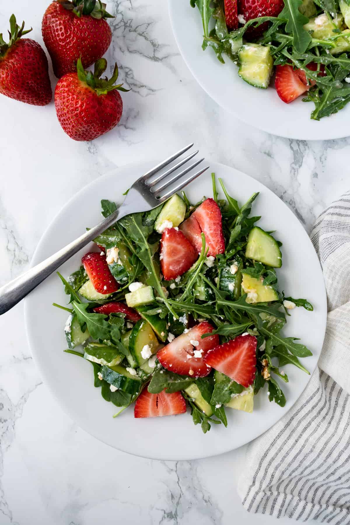 Cucumber Strawberry Salad with Arugula on a salad plate with a fork.