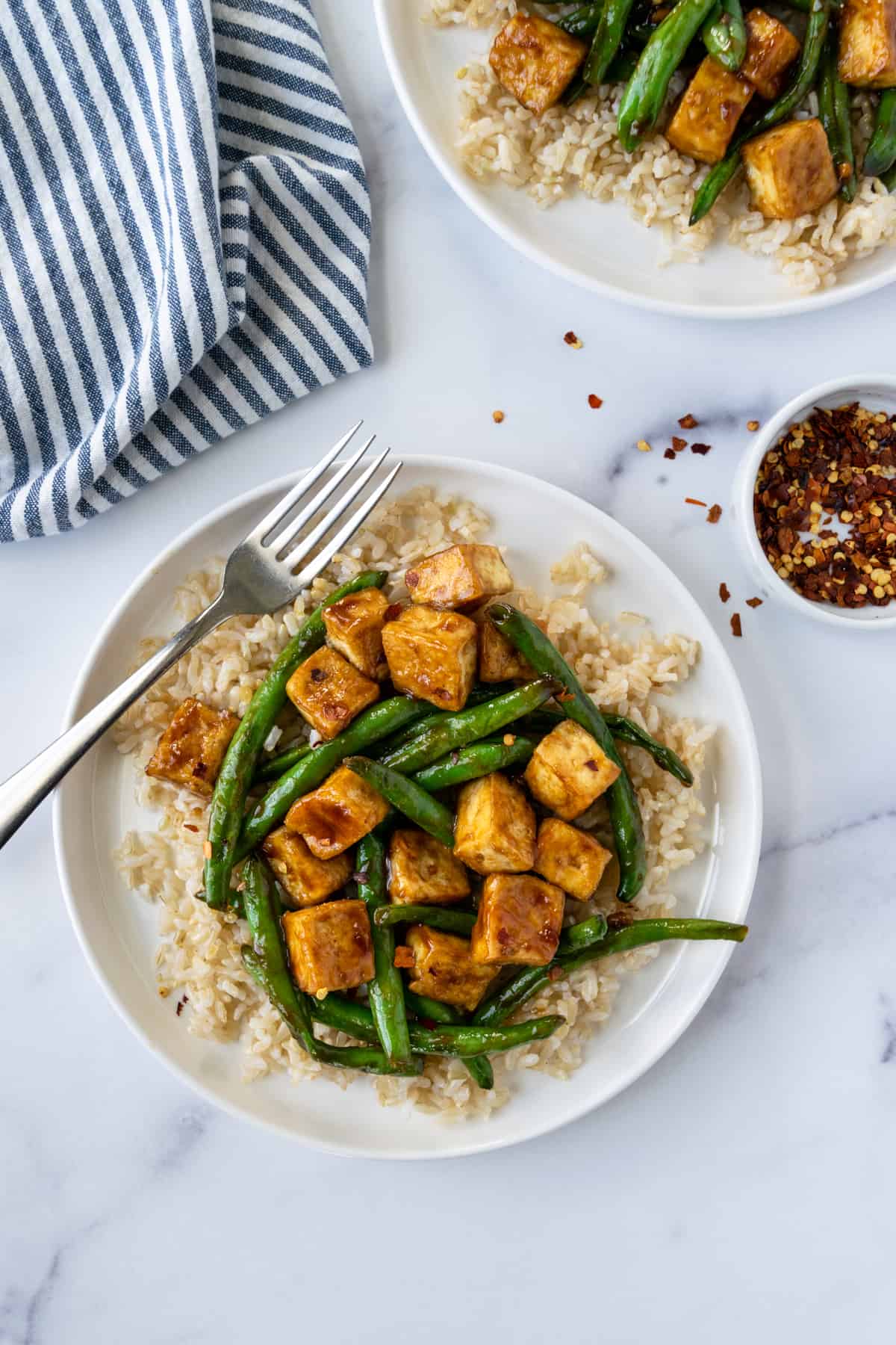 Teriyaki Tofu Stir Fry with Green Beans on a white plate with crushed red pepper.