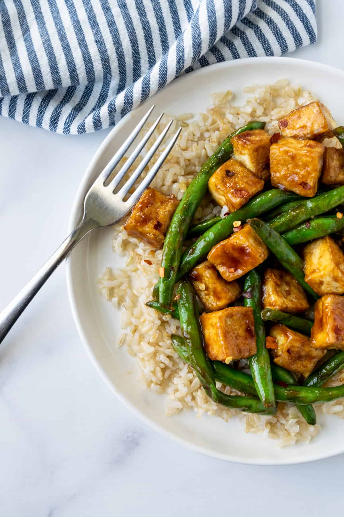 Teriyaki Tofu Stir Fry with Green Beans on a white plate on a table with a blue and white striped linen.