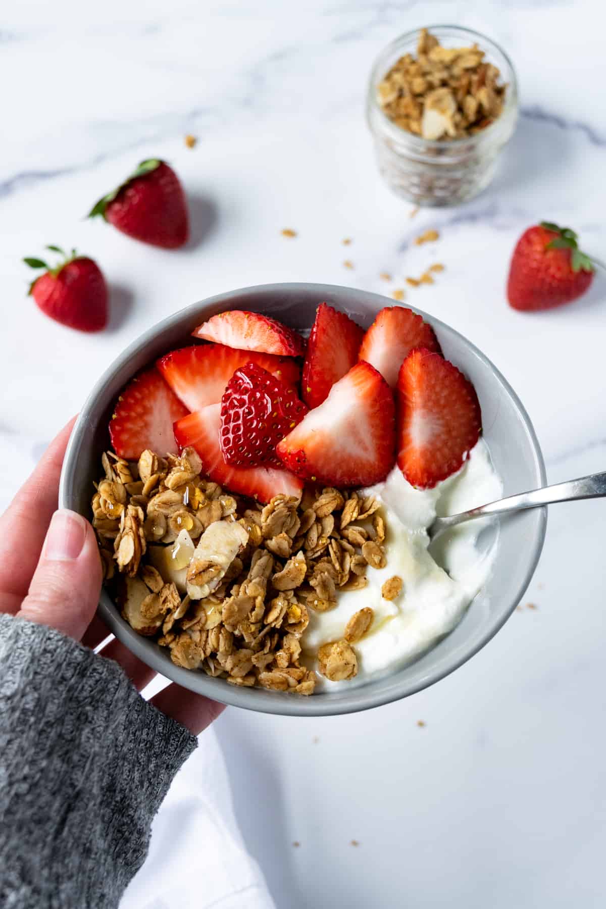A person holding a Yogurt Granola Bowl with strawberries.