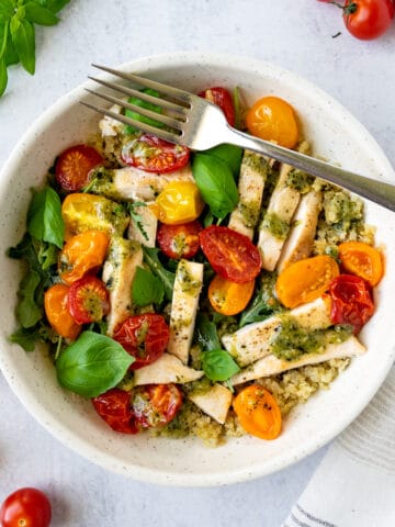 Pesto Chicken Quinoa Bowl on a table with cherry tomatoes and basil.