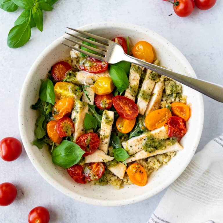 Pesto Chicken Quinoa Bowl on a table with cherry tomatoes and basil.