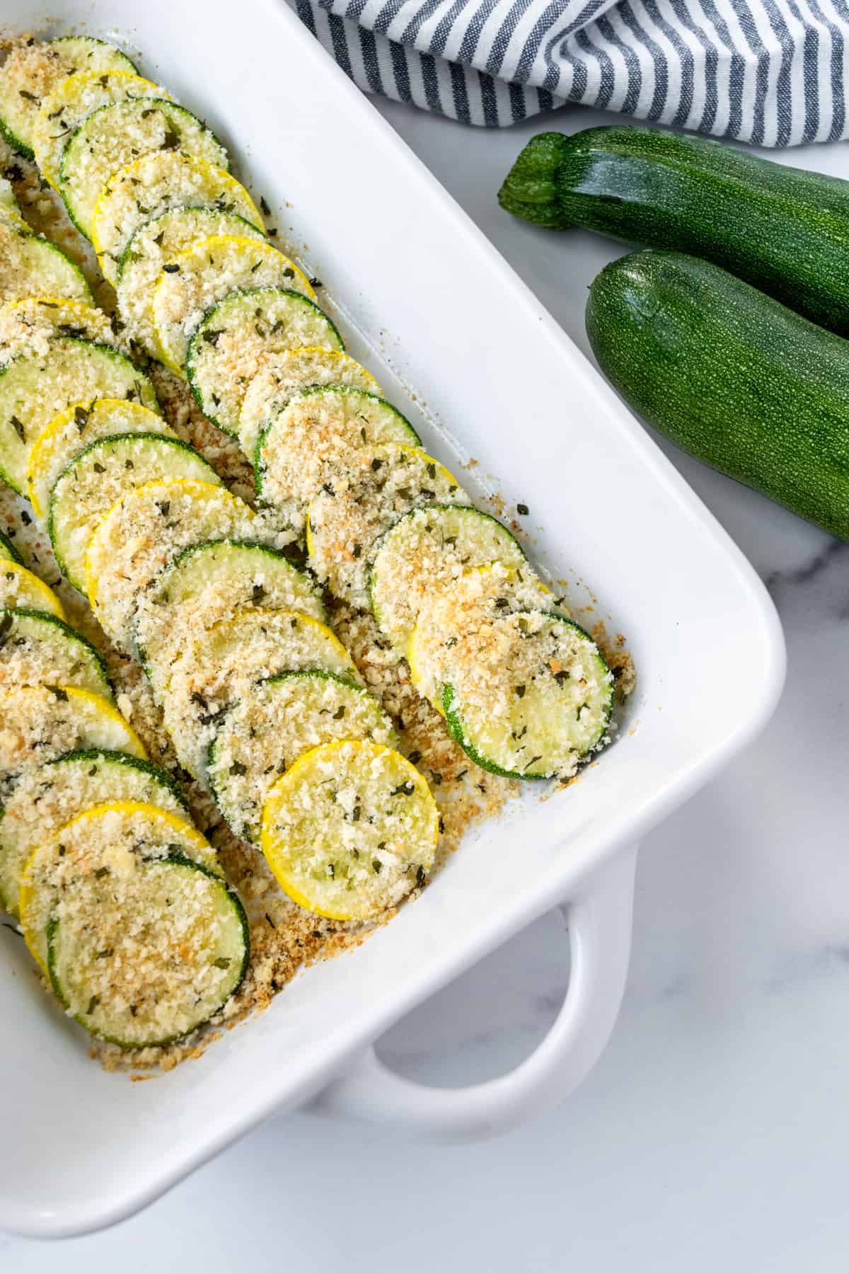 Zucchini and Squash Bake in a casserole dish with fresh zucchini on the table next to it.