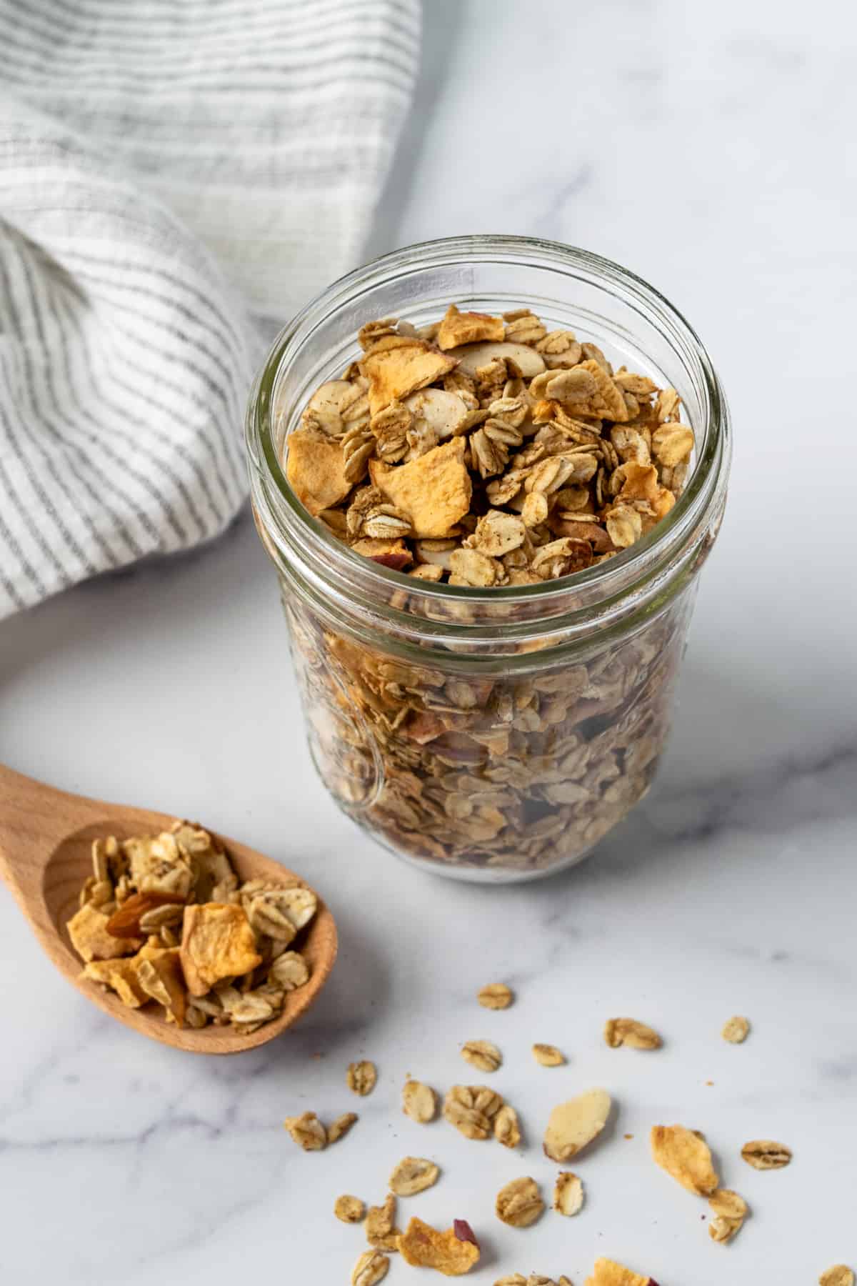 Apple Cinnamon Granola in a glass jar with a wooden spoon.