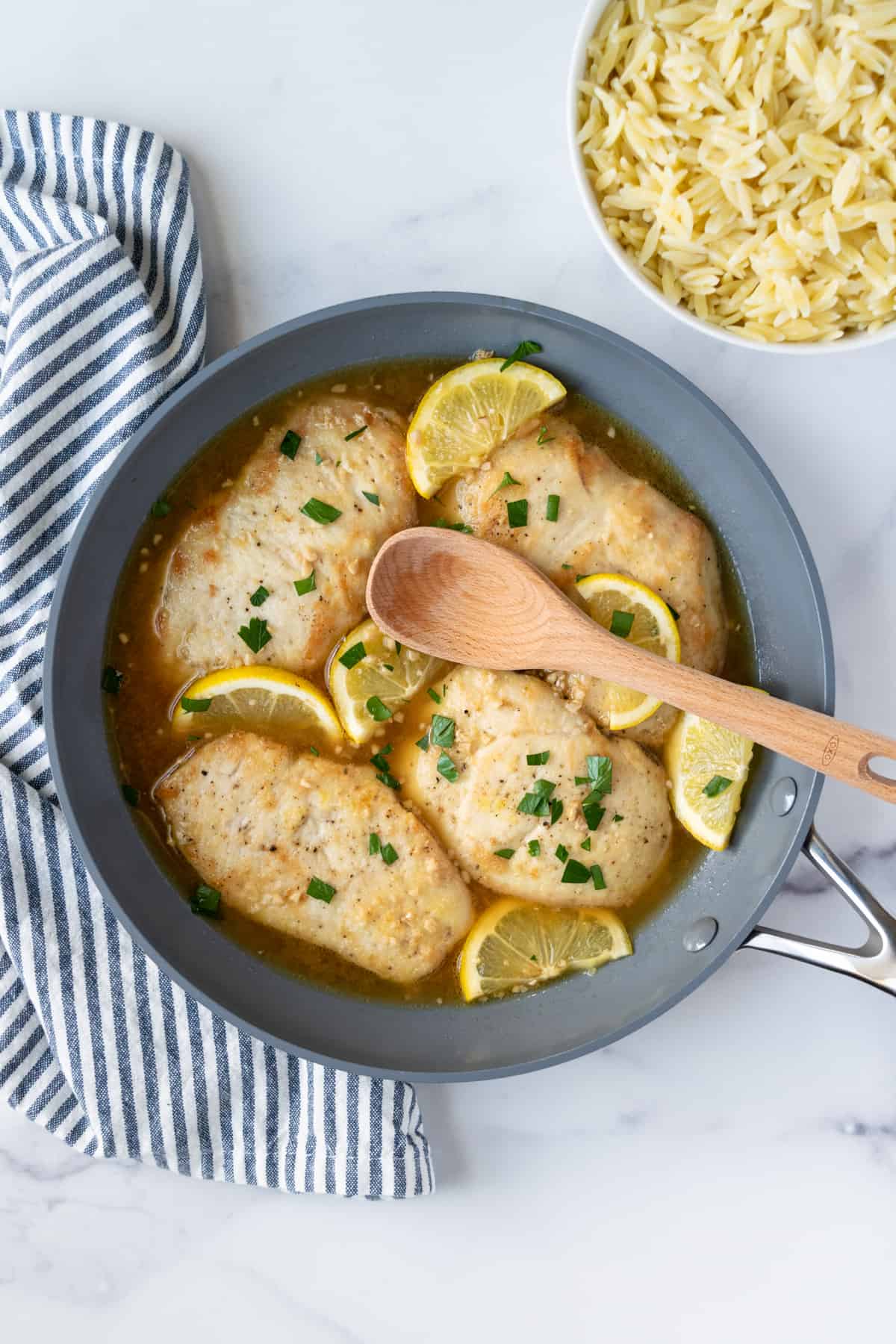 Honey Garlic Lemon Chicken in a skillet with a bowl of orzo next to it.
