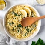 Lemon Orzo with Spinach in a white bowl with a wooden serving spoon.