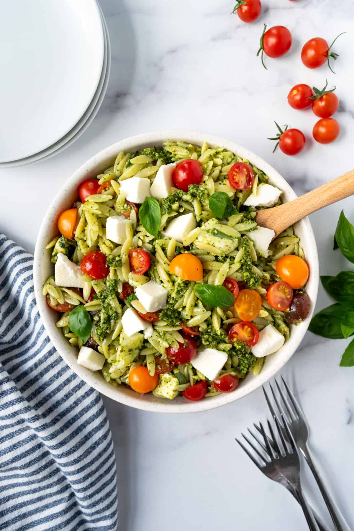 Pesto Orzo Salad in a white bowl with a wooden spoon.