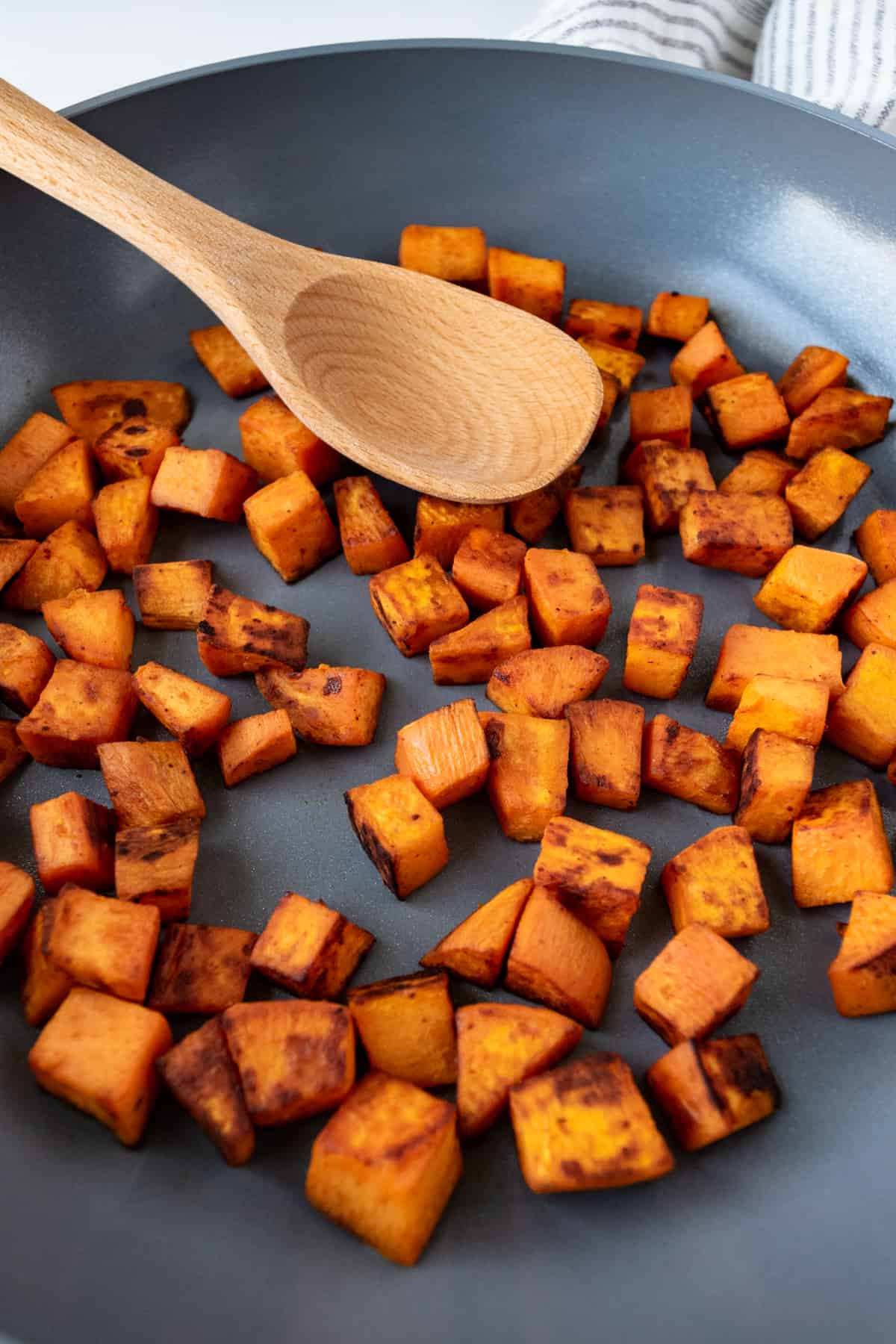 Sautéed Sweet Potatoes in a skillet with a wooden spoon.