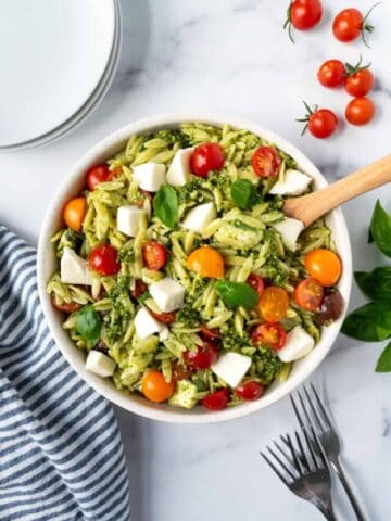 Pesto Orzo Salad in a white bowl with a wooden spoon.