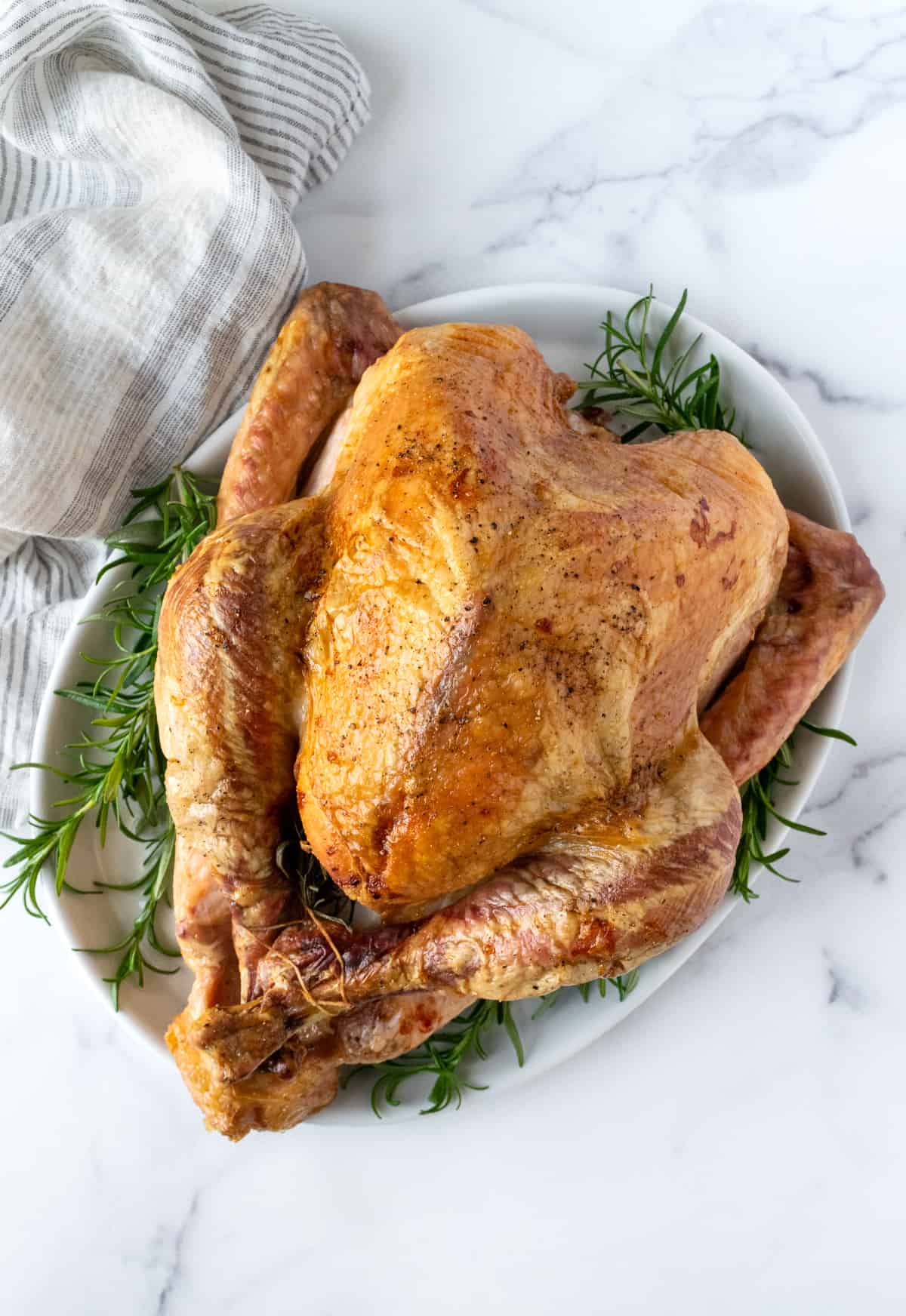 Easy Roast Turkey on a white platter with rosemary sprigs.