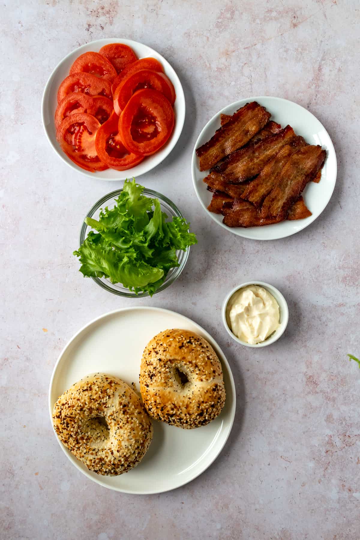 White plates of cooked bacon, lettuce, tomatoes, mayo and bagels.