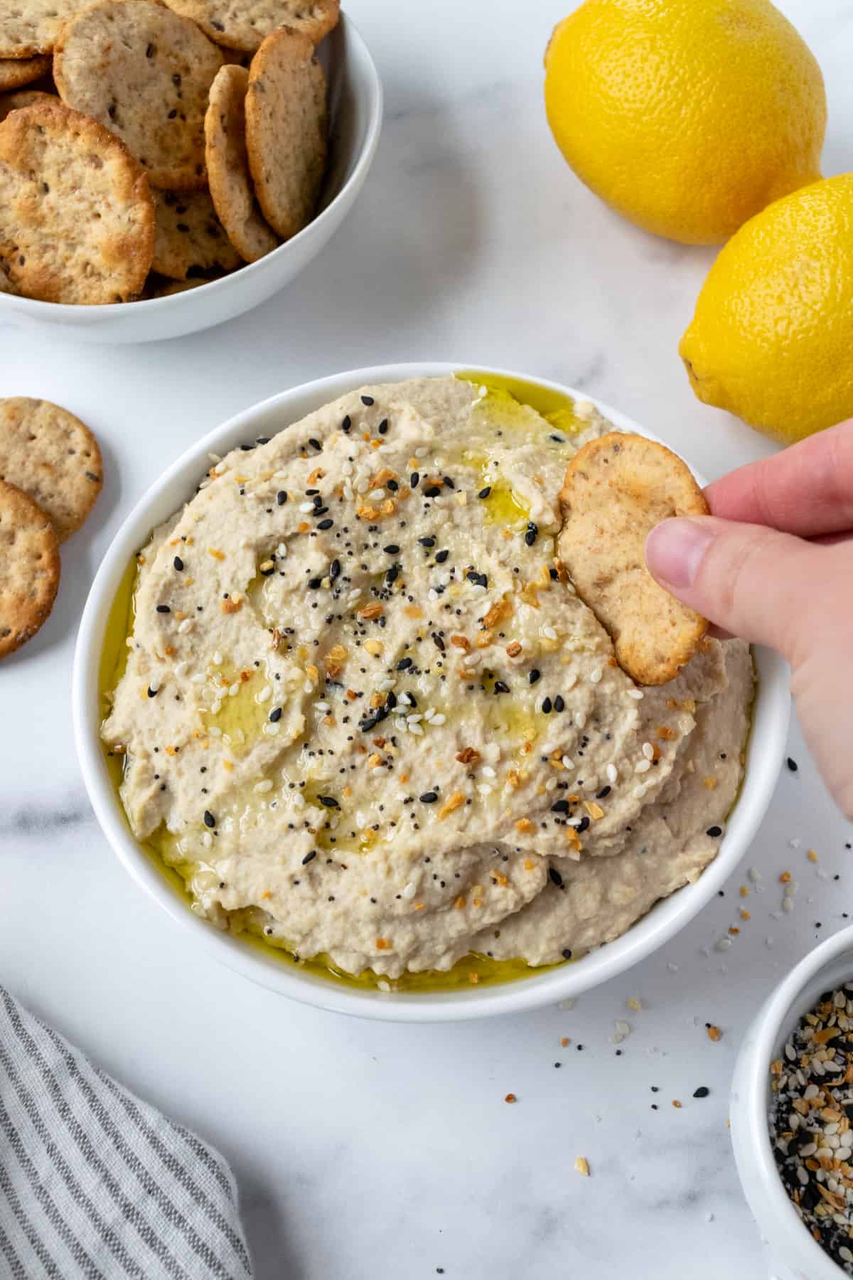 Everything Bagel Hummus with a hand dipping a cracker in it.