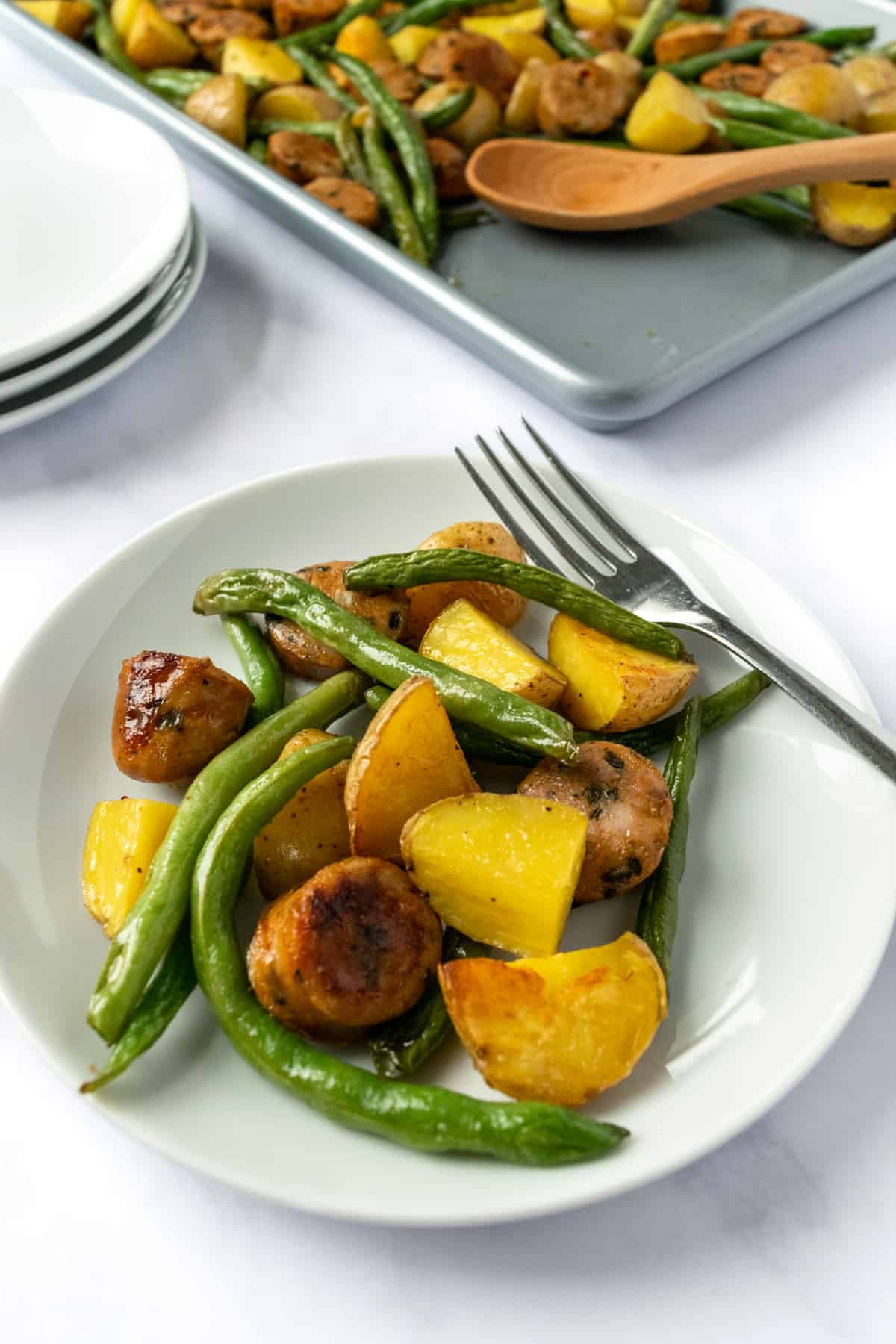 Green Beans with Potatoes and Sausage on a white plate with a fork.
