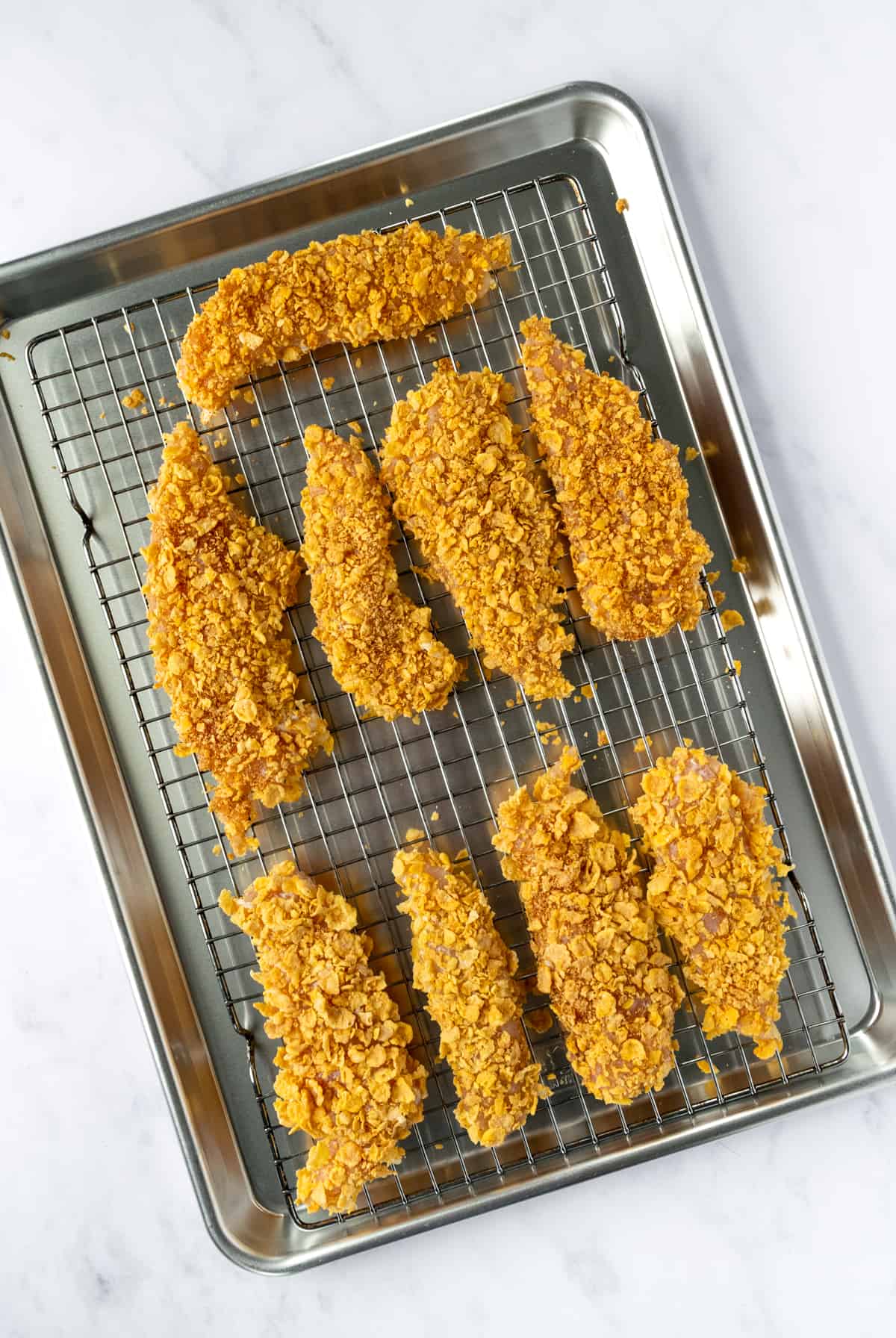 Cornflake Chicken Tenders on a white rack on a baking sheet.