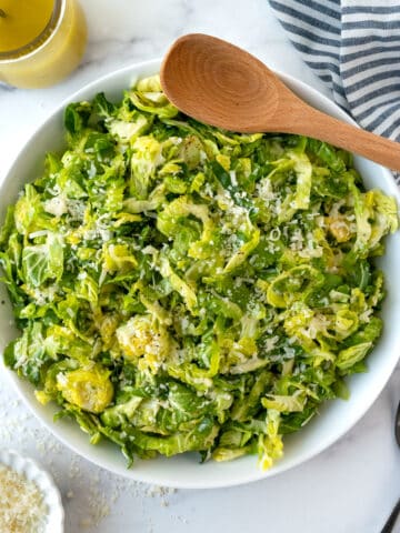 Parmesan Brussels Sprouts Salad in a serving bowl with a wooden spoon.