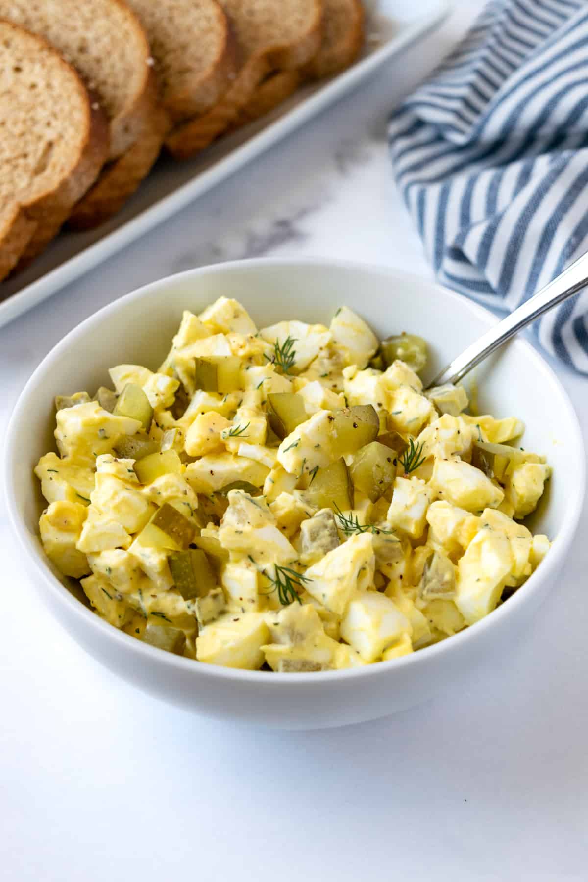 Egg Salad with Pickles in a white bowl with a serving spoon.