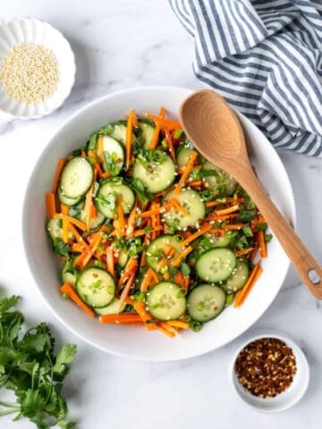 Cucumber Carrot Salad in a white bowl with a wooden spoon.
