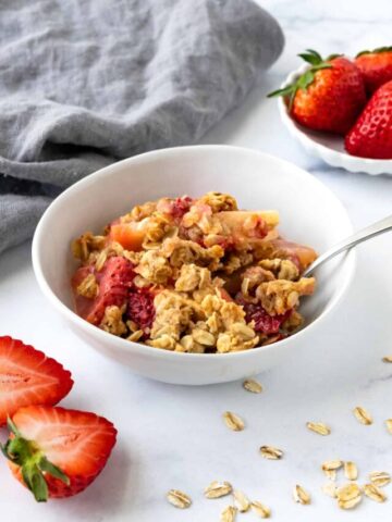 Strawberry Apple Crisp in a white bowl with a spoon.