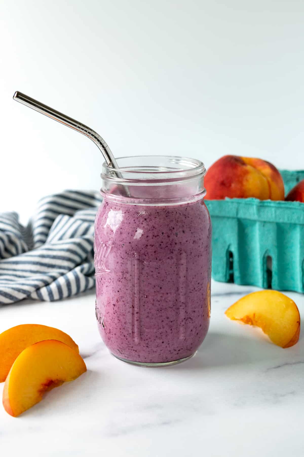 Blueberry Peach Smoothie in a mason jar with a metal straw.