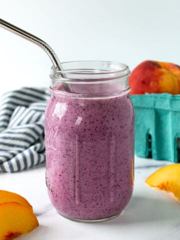 Blueberry Peach Smoothie in a mason jar on a marble countertop with peach slices next to it.