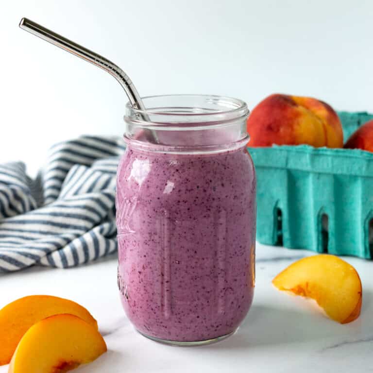 Blueberry Peach Smoothie in a mason jar on a marble countertop with peach slices next to it.