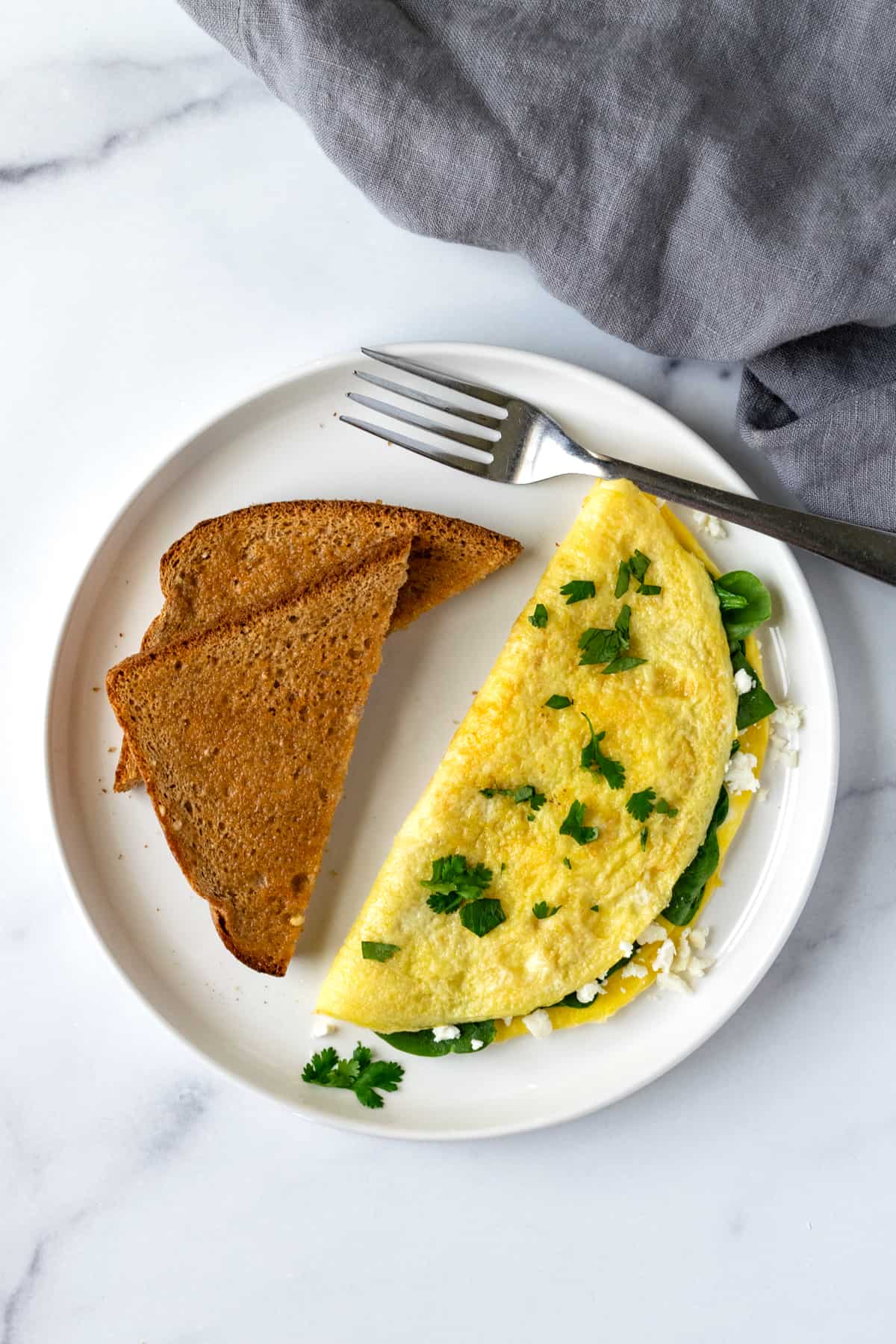 Omelette with Spinach and Feta on a white plate with toast with a fork.