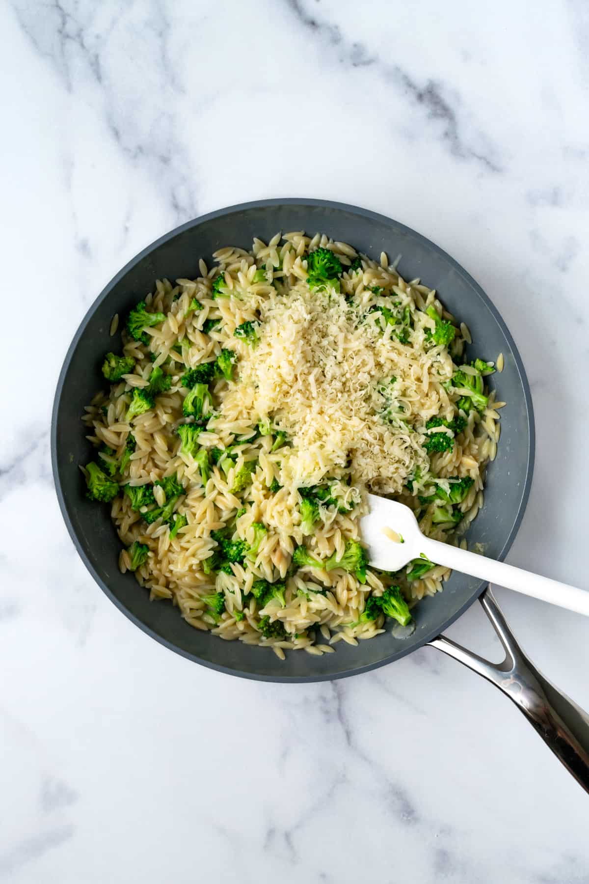 A skillet with a spatula stirring in cheese into broccoli cheddar orzo.