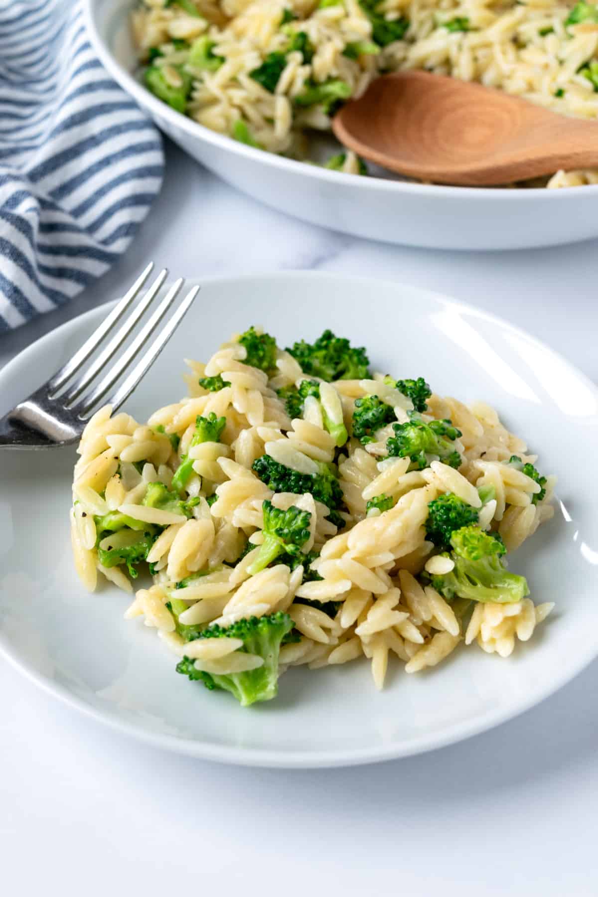 Broccoli Cheddar Orzo on a white plate with a fork.
