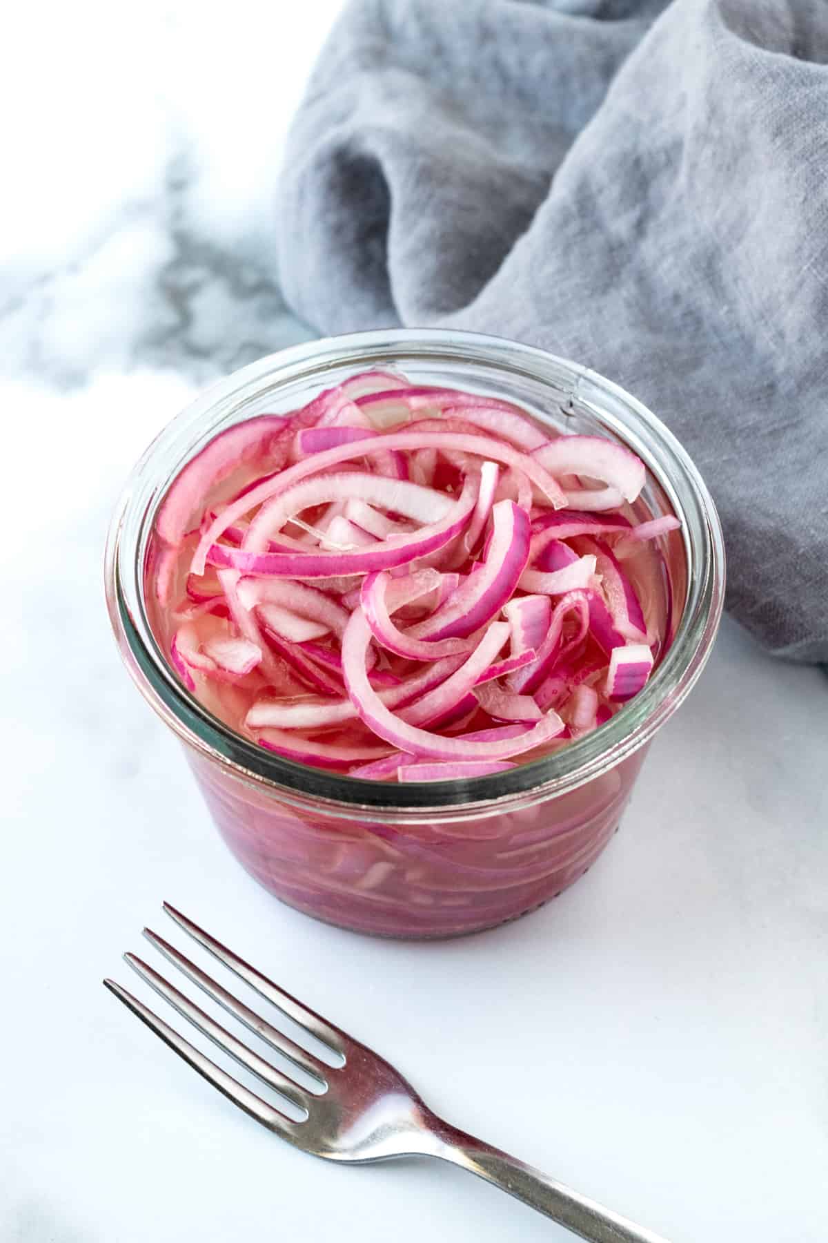 Quick Pickled Onions in a Glass Jar on a marble countertop.