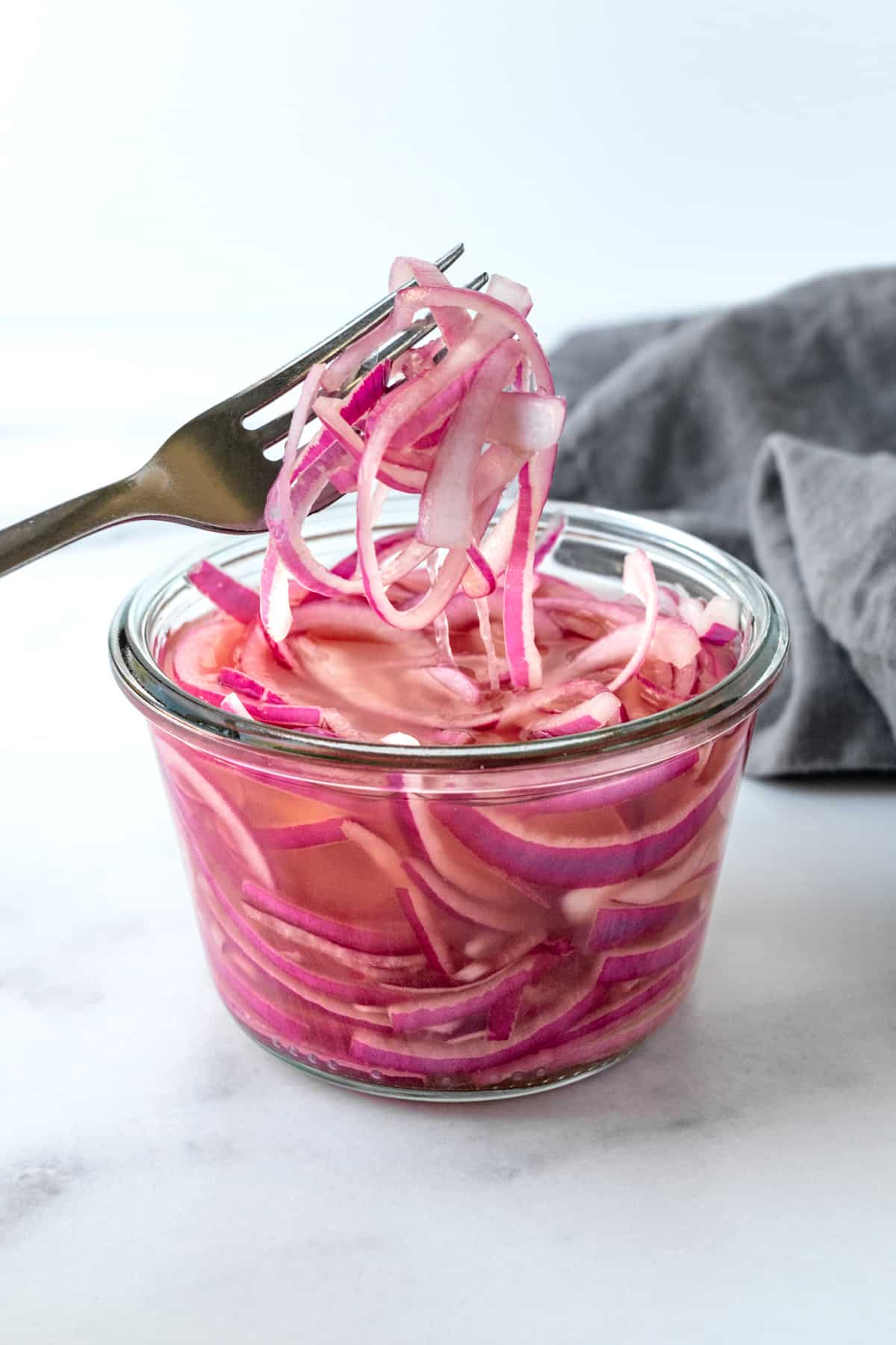 Quick Pickled Red Onions with a fork on a marble countertop.
