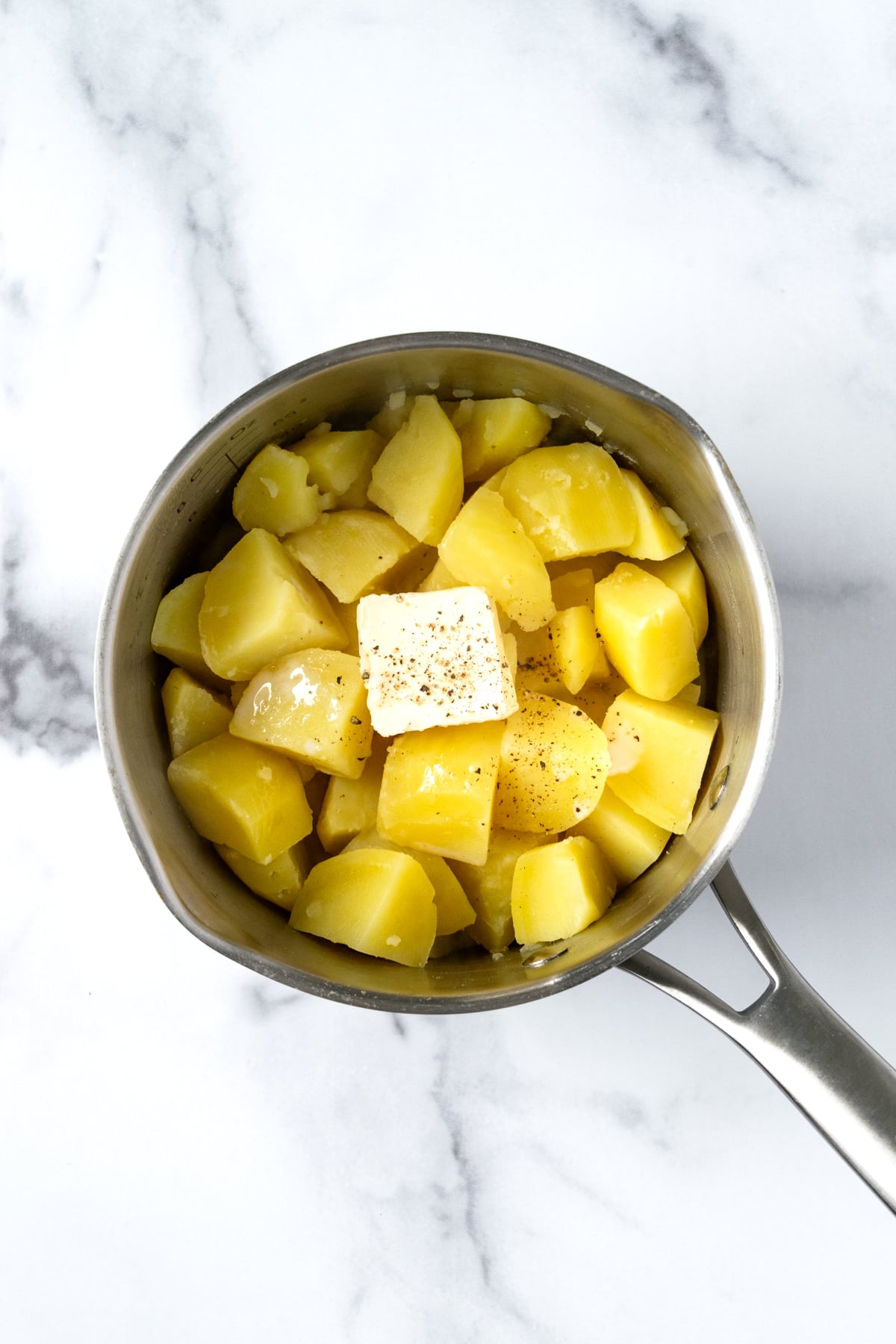 Cooked potatoes in a pot with plant-based butter and almond milk ready to be mashed.