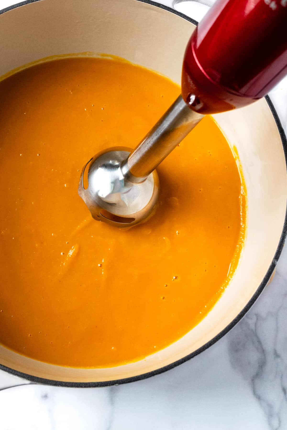 Immersion blender blending squash soup in a white pot.